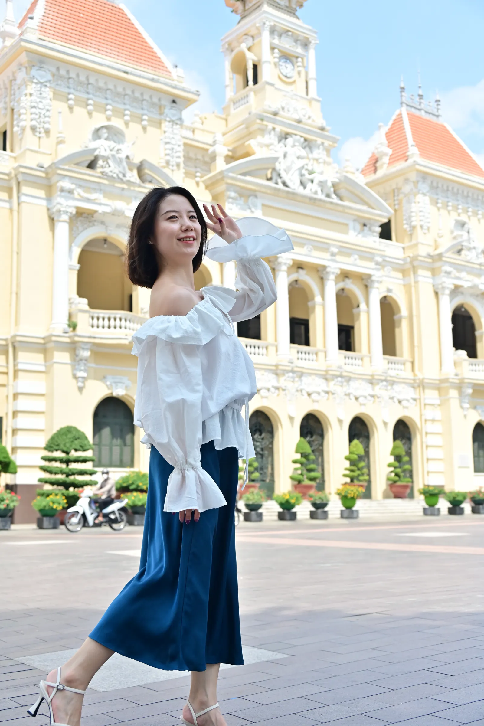 Woman walking in front of the yellow colonial City Hall in Ho Chi Minh City